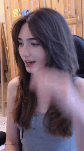 A Woman In A Blue Tank Top Is Sitting In Front Of A Wooden Door GIF