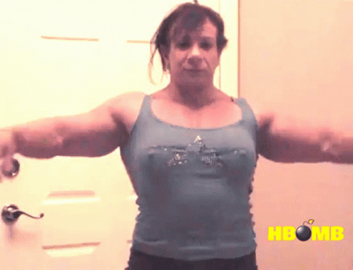 A Woman In A Blue Tank Top Is Standing In Front Of A Door With The Word Hbomb On The Bottom GIF