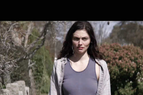 A Woman In A Blue Tank Top Stands In Front Of Bushes GIF