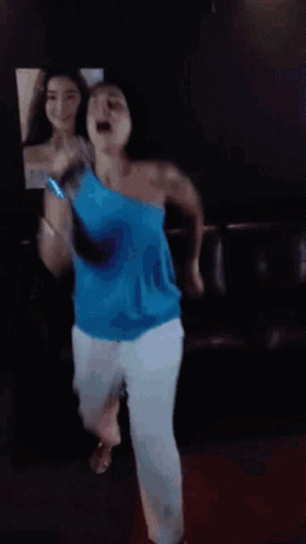 a woman in a blue top is dancing in front of a mirror