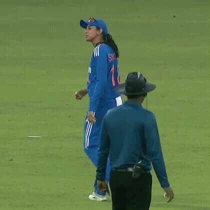 A Woman In A Blue Uniform Is Walking On A Cricket Field Next To A Referee . GIF