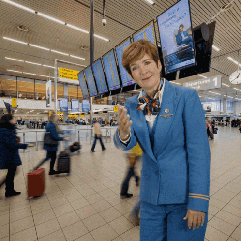 A Woman In A Blue Uniform Stands In Front Of A Sign That Says Departures Week GIF