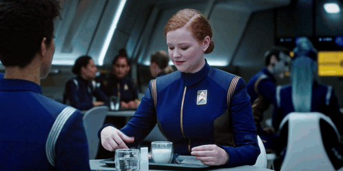 A Woman In A Blue Uniform With A Badge That Says ' Star Trek ' On It GIF