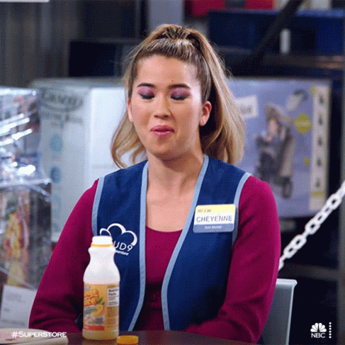 A Woman In A Blue Vest Is Sitting At A Table With A Bottle Of Orange Juice In Front Of Her . GIF