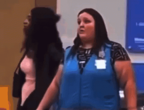 A Woman In A Blue Vest Is Standing Next To Another Woman In A Room . GIF