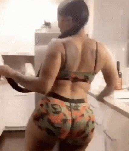 A Woman In A Bra And Shorts Is Standing In A Kitchen Holding A Knife . GIF