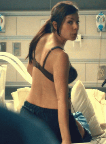 A Woman In A Bra Is Sitting On A Bed In A Hospital Room GIF