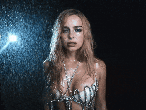 A Woman In A Bra With Pearls On It Is Standing In The Rain GIF