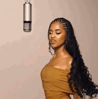 A Woman In A Brown Dress Is Standing In Front Of A Microphone . GIF