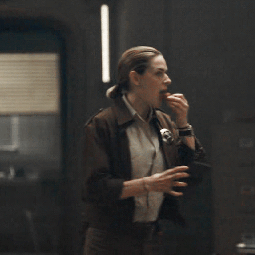 A Woman In A Brown Jacket Is Eating Something While A Man Looks On GIF