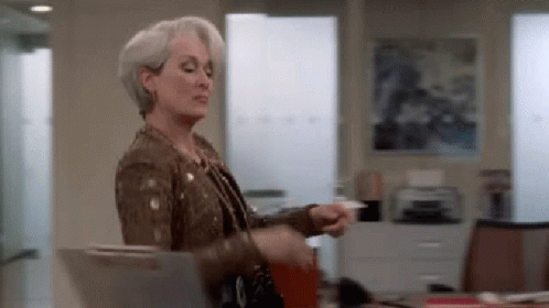 A Woman In A Brown Jacket Is Holding A Piece Of Paper In Her Hand . GIF
