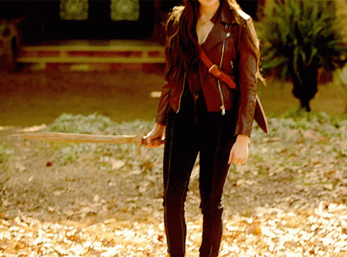 A Woman In A Brown Leather Jacket Holds A Wooden Stick GIF