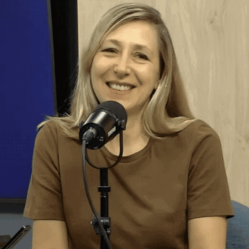 A Woman In A Brown Shirt Is Smiling In Front Of A Black Microphone GIF