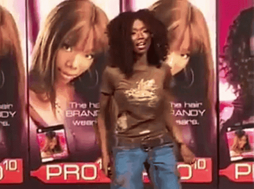 A Woman In A Brown Shirt Is Standing In Front Of A Row Of Advertisements For Pro GIF