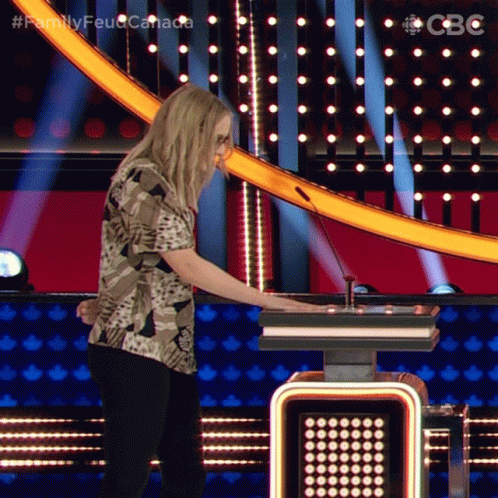 A Woman In A Camo Shirt Is Playing A Game On A Stage With The Words Family Feud Canada On The Bottom GIF