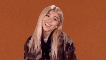 A Woman In A Camouflage Jacket Is Making A Funny Face And Giving A Thumbs Up . GIF
