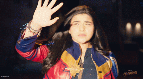 A Woman In A Captain Marvel Costume Is Waving GIF