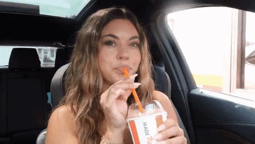 A Woman In A Car Drinking Through A Straw From A Cup That Says Made GIF