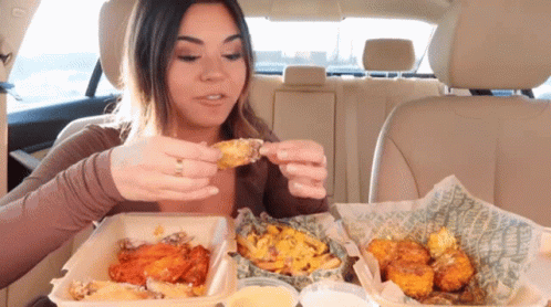 A Woman In A Car Is Eating Chicken Wings GIF