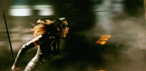 A Woman In A Catwoman Costume Is Running Through A Dark Room . GIF