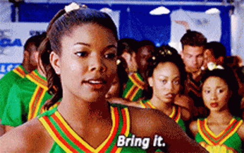 A Woman In A Cheerleading Uniform Is Standing In Front Of A Crowd Of People . GIF