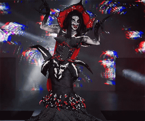 A Woman In A Clown Costume Is Standing On A Stage With Her Arms Outstretched GIF