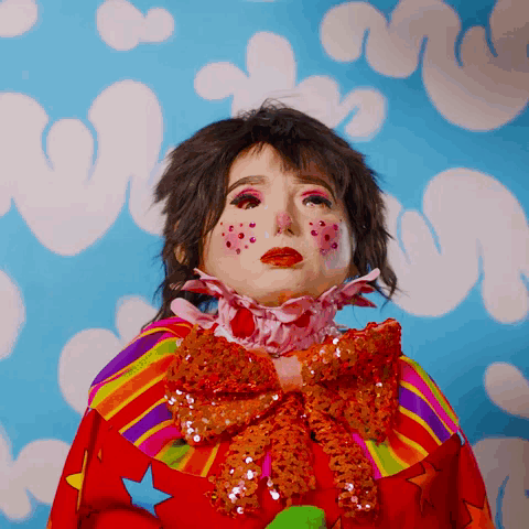 A Woman In A Clown Costume With A Rainbow Collar And Bow GIF