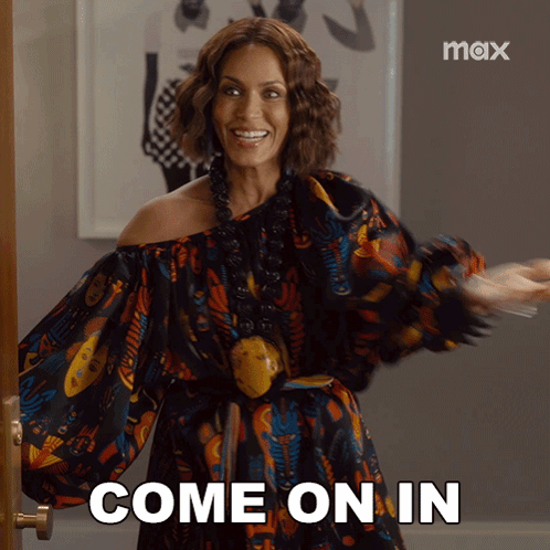 A Woman In A Colorful Dress Is Standing In Front Of A Door And Says Come On In GIF