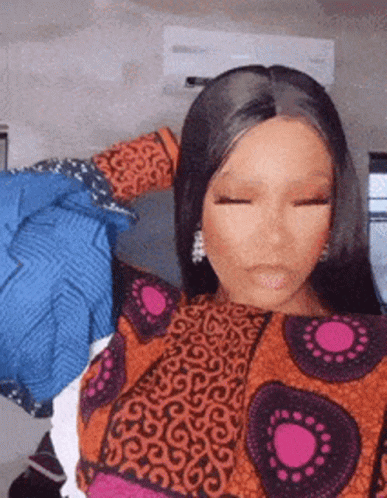 A Woman In A Colorful Dress Is Standing In Front Of A Wall With Clothes On It . GIF