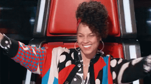 A Woman In A Colorful Jacket Is Sitting In A Chair With Her Arms Outstretched And Smiling . GIF