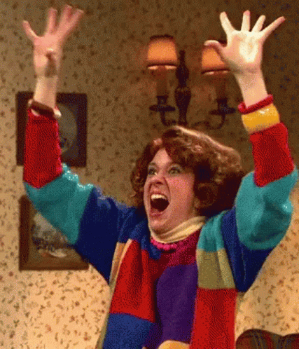 A Woman In A Colorful Sweater Has Her Arms In The Air GIF