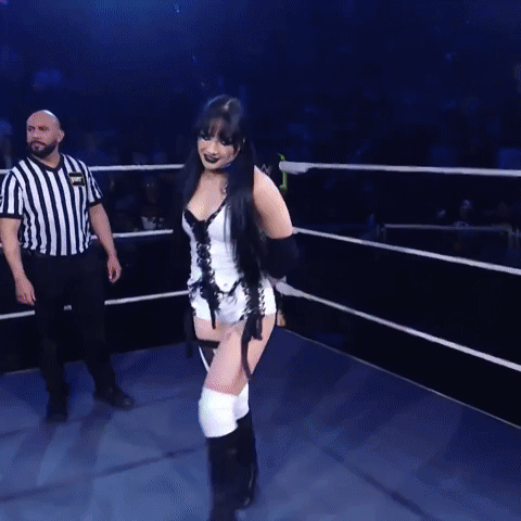 A Woman In A Corset Is Walking In A Ring With A Referee GIF