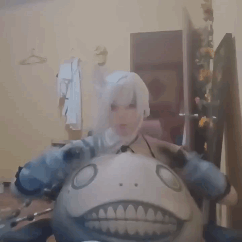 A Woman In A Cosplay Costume Is Holding A Stuffed Animal With A Big Mouth . GIF