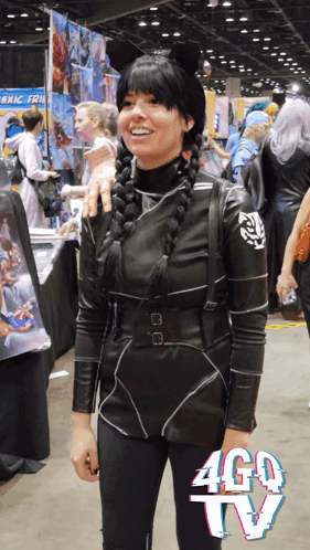 A Woman In A Costume Stands In Front Of A Sign That Says Ago Tv GIF