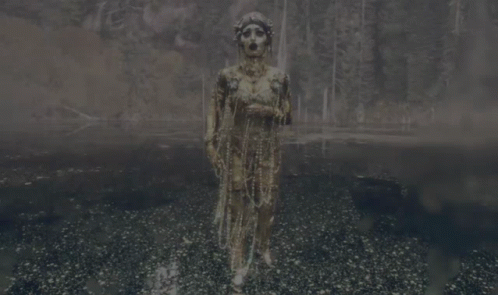 A Woman In A Costume With Pearls Hanging From Her Neck GIF
