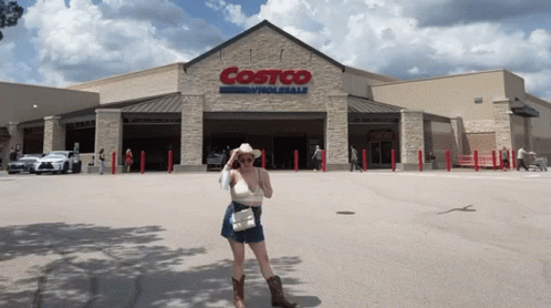 A Woman In A Cowboy Hat Stands In Front Of A Costco Wholesale Store GIF
