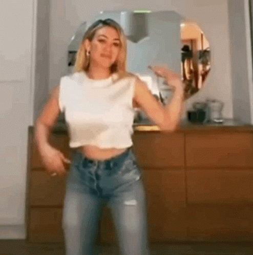 A Woman In A Crop Top And Jeans Is Dancing In A Kitchen . GIF