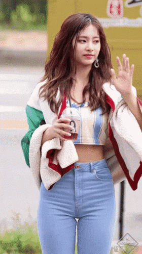 A Woman In A Crop Top And Jeans Is Holding A Drink GIF