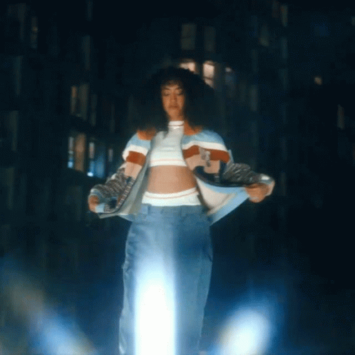 A Woman In A Crop Top And Jeans Is Standing In Front Of A Building GIF
