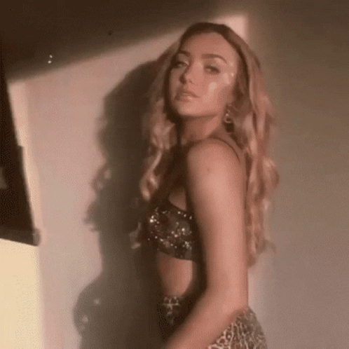 A Woman In A Crop Top And Leopard Print Skirt Is Standing In Front Of A White Wall . GIF