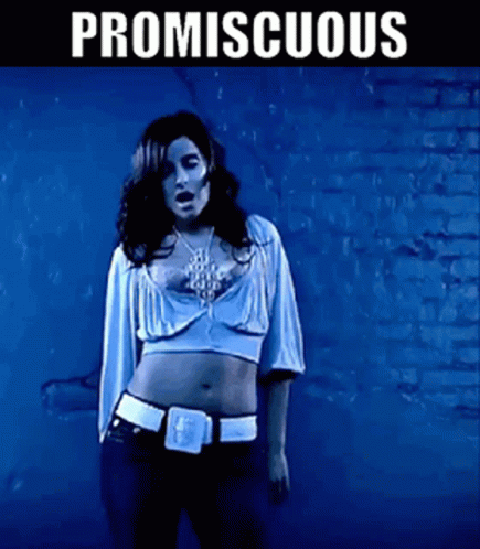 A Woman In A Crop Top Is Standing In Front Of A Brick Wall With Promiscuous Written On It GIF