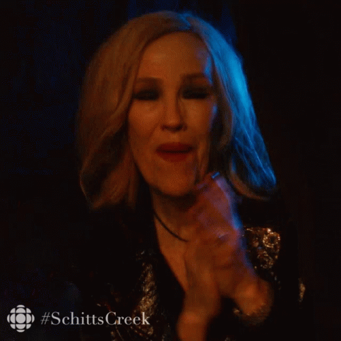 A Woman In A Dark Room With #Schittscreek Written On The Bottom Right GIF