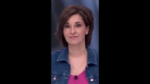 a woman in a denim jacket and a pink shirt is smiling .