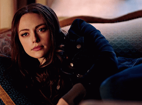 A Woman In A Denim Jacket Is Laying On A Couch Looking At The Camera GIF