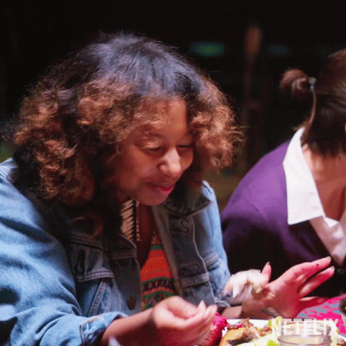 A Woman In A Denim Jacket Is Sitting At A Table With A Plate Of Food GIF
