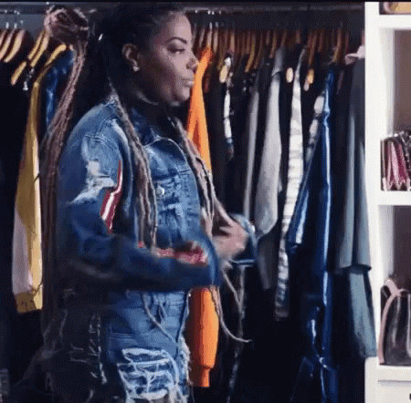 A Woman In A Denim Jacket Is Standing In Front Of A Closet Filled With Clothes . GIF