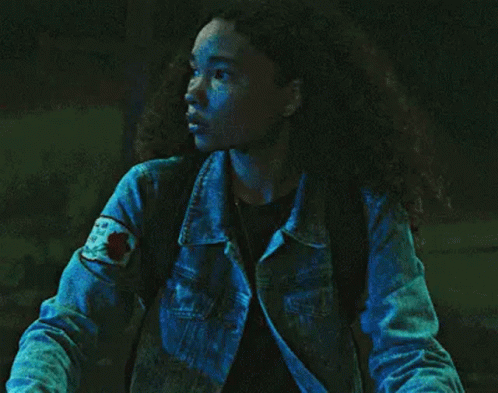 a woman in a denim jacket is standing in the dark .
