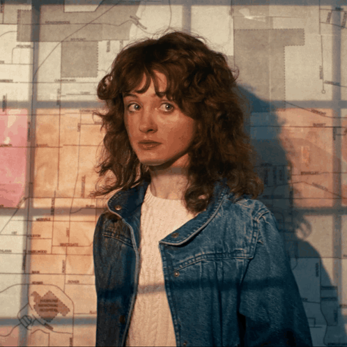 A Woman In A Denim Jacket Stands In Front Of A Map That Says The T On It GIF