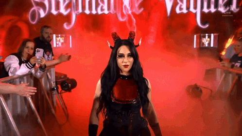 A Woman In A Devil Costume Stands In Front Of A Sign That Says ' Stephanie Vaughn ' GIF