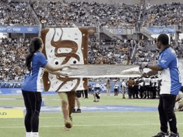 A Woman In A Donut Costume Is Holding A Large Donut On A Field GIF